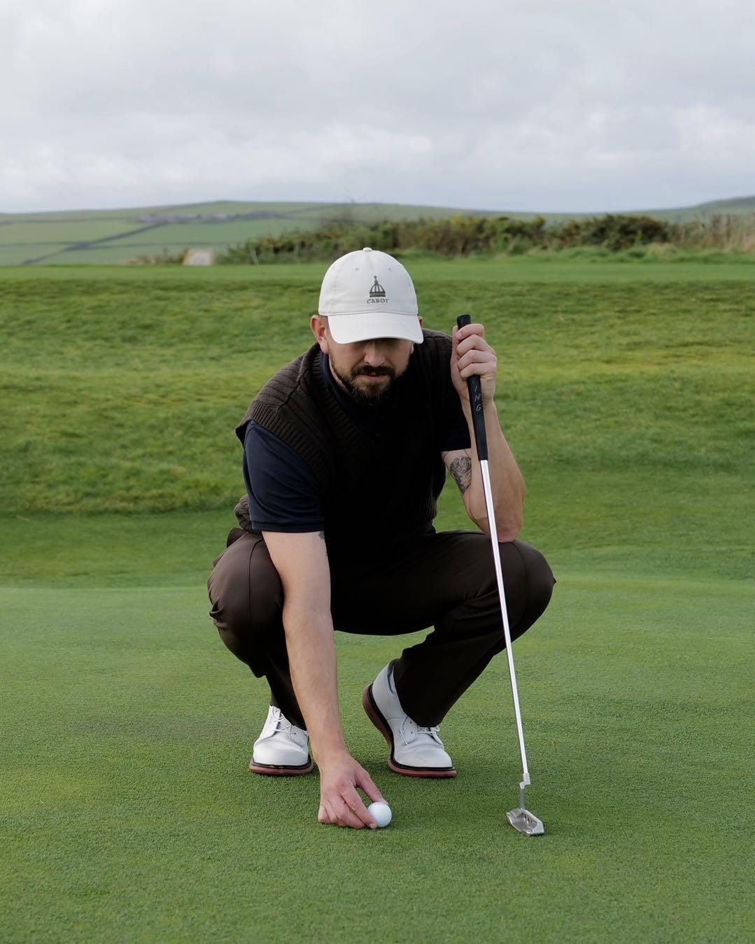 A person in a white hat and vest holding a golf club

Description automatically generated