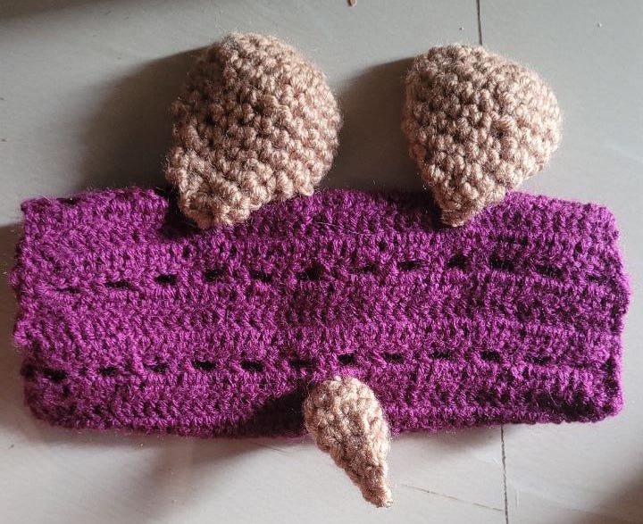 A purple crocheted pouch with brown dog ears and a tail.