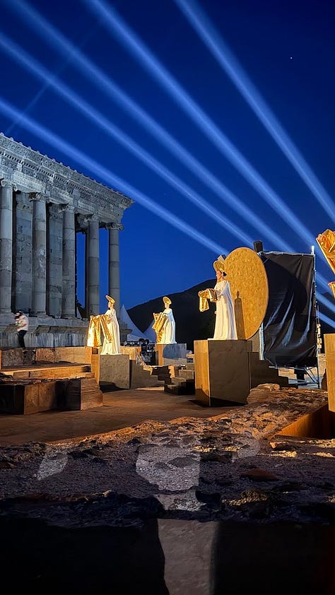Photos from the Concours Mondial de Bruxelles cultural program in Armenia, including a group dinner at a long candlelit table, a meeting room with the Armenian minister of economy beneath the national flag, a display of Soviet-era wine industry memorabilia and archival photos, aging wine barrels in a cellar, a group photo overlooking Yerevan with Mount Ararat in the distance, illuminated performers at the Garni Temple at night, traditional dancers performing acrobatics, a crowd joining a folk dance circle outdoors, and a large karas amphora covered in visitor signatures." Let me know if you'd like it trimmed or reordered to lead with a particular image.
