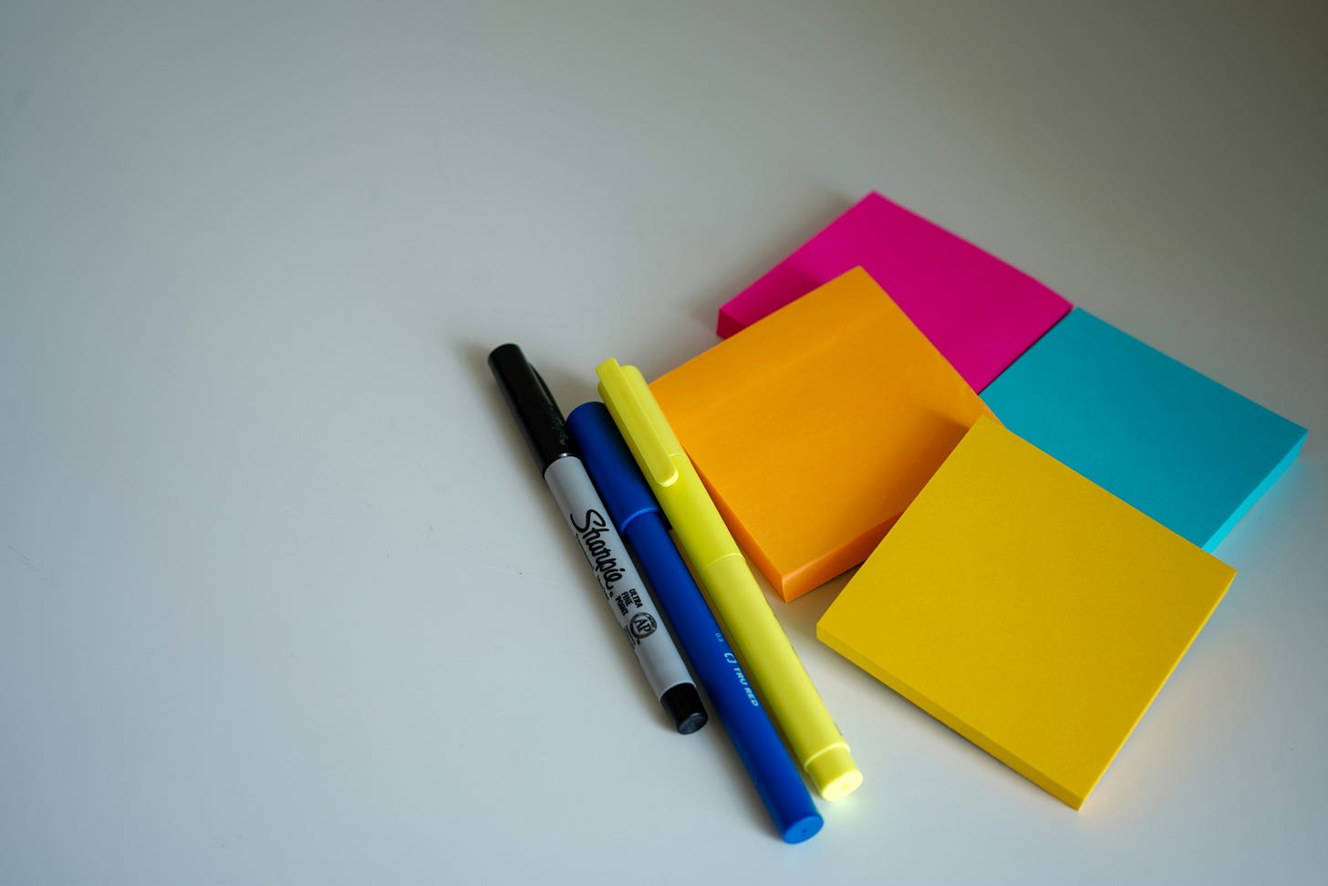 Neon post it notes next to a collection of pens