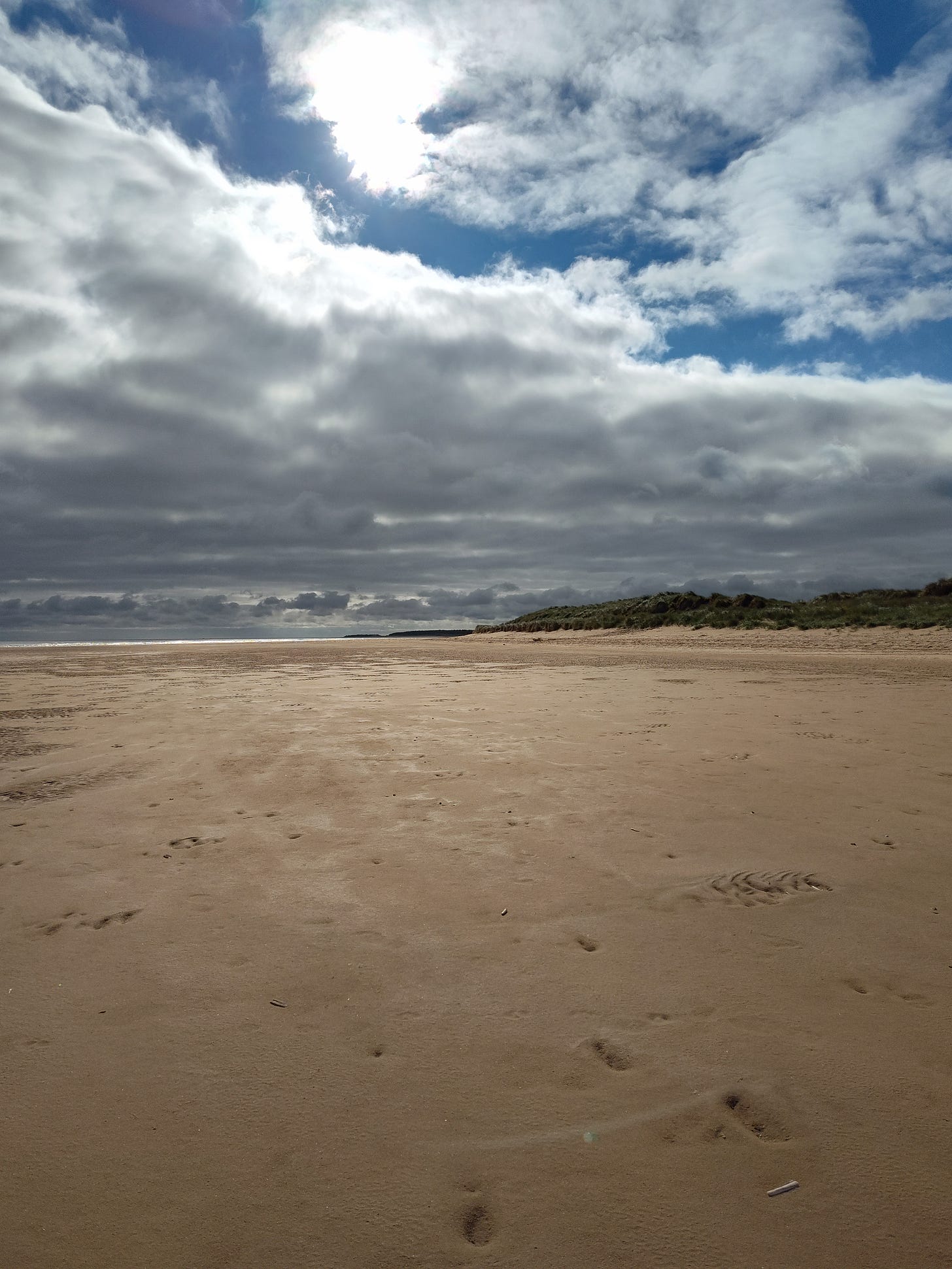 Dramatic clouds over an expanse of sand, a little water in the distance.