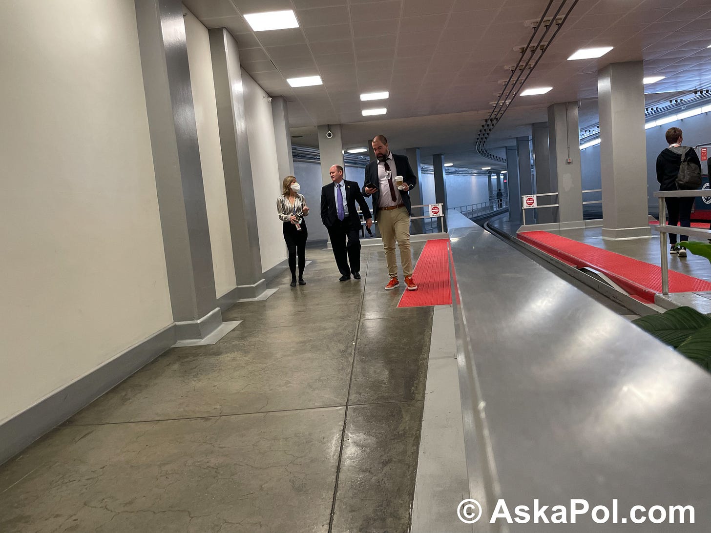 In an underground tram tunnel a female reporter asks a male Senator in a suit questions as a male reporter looks at his phone. Photo: Matt Laslo 