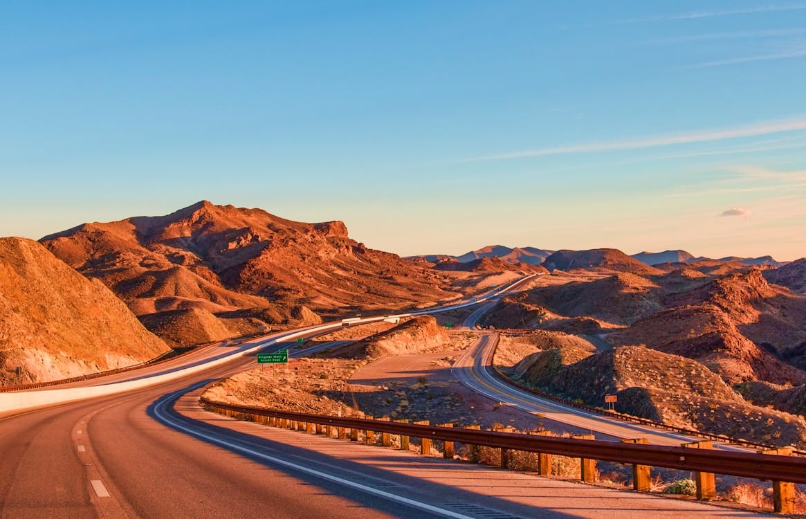 Free Stunning view of a winding highway amidst Nevada's rugged landscape under blue skies at sunset. Stock Photo