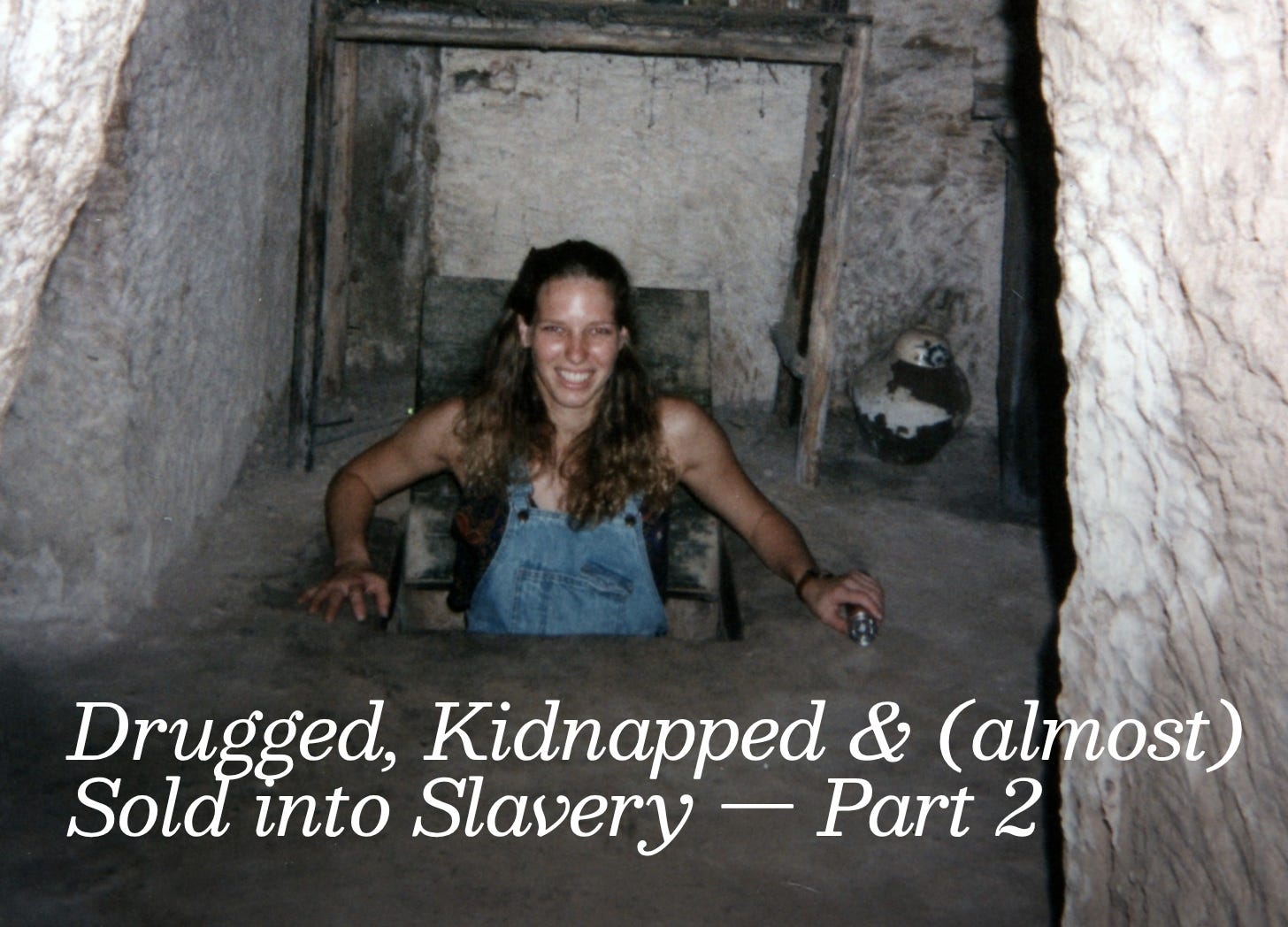 A young white woman with long blond hair is wearing jean overalls and popping out of a hole in a dirt dungeon underground. She is smiling like an idiot, unaware of her surroundings.