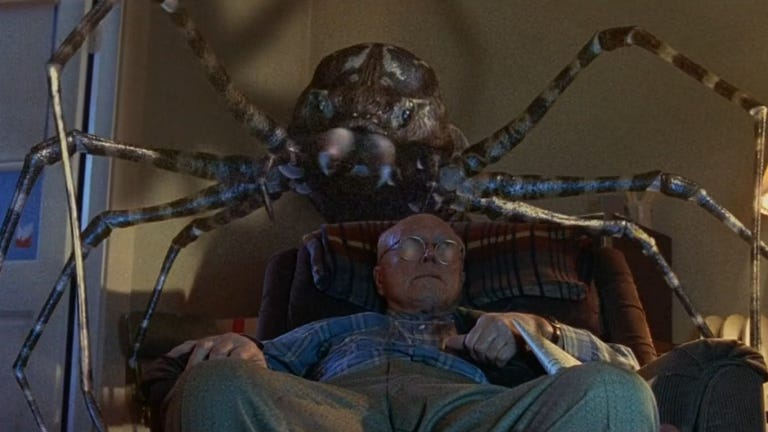 A giant spider looms over a older man sitting in an easy chair.