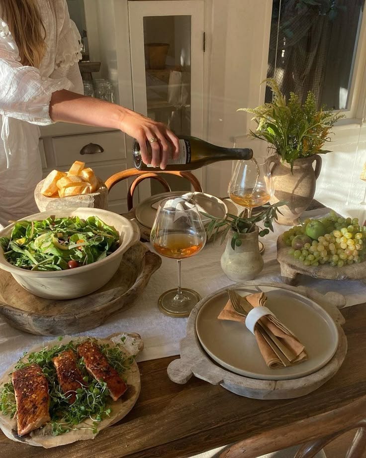 This may contain: a woman pours wine into a bowl filled with salad and other foods on a table