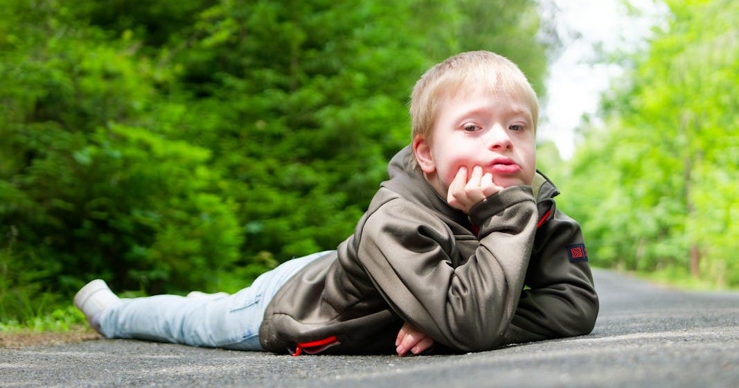 Young boy lying on a path in the woods