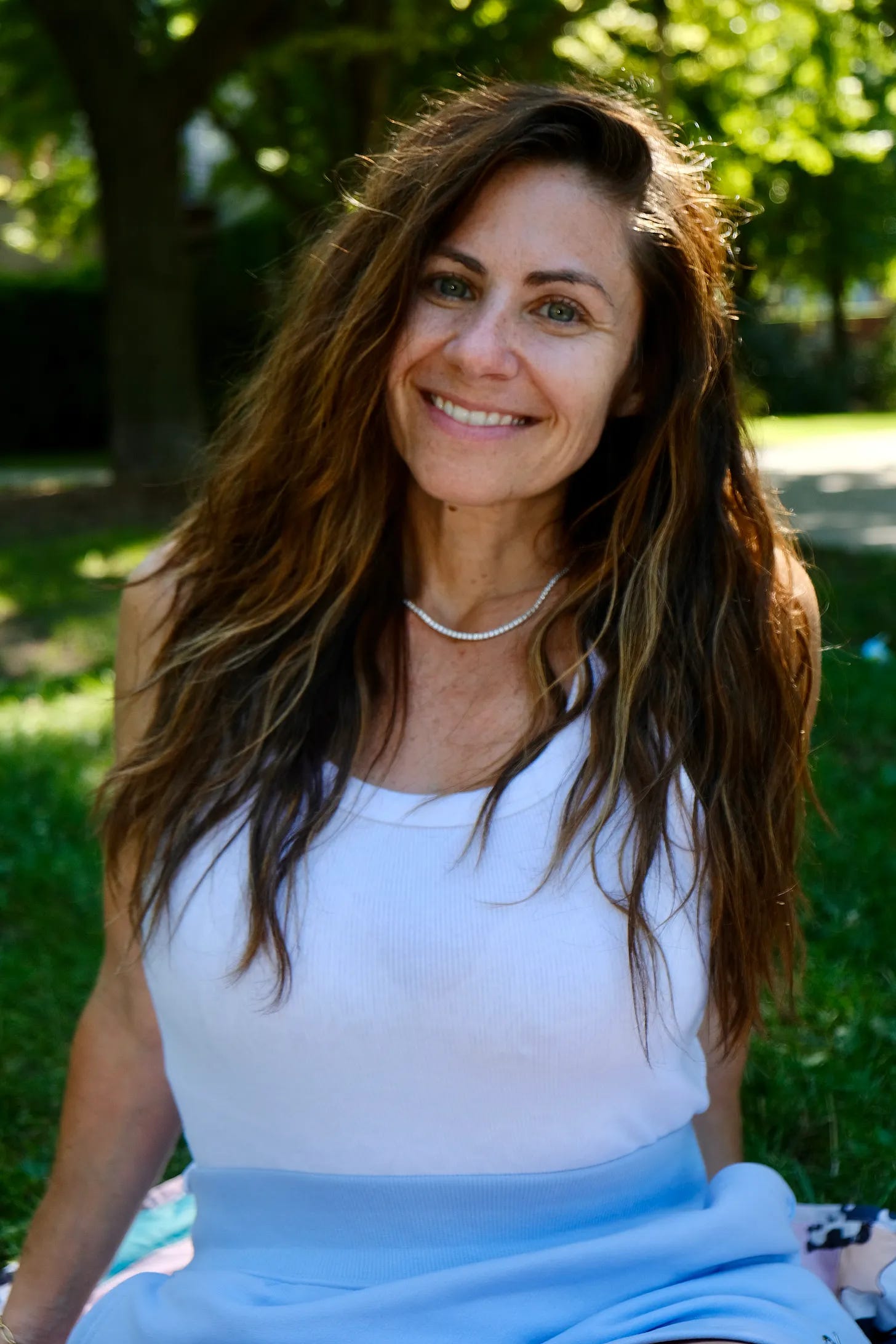 a photo of Christina Nikols Energy Healer looking happier than ever in a park, smiling in the sunshine in a periwinkle skirt and a white tank top periwinkle skirt from aloe white tank top from target and a diamond necklace a photo of Christina Nikols Energy Healer looking happier than ever in a park, smiling in the sunshine in a periwinkle skirt and a white tank top periwinkle skirt from aloe white tank top from target and a diamond necklace