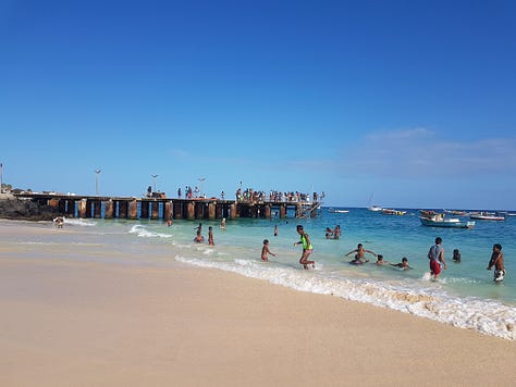 A wooden pier stretching into bright turquoise water, with small waves rolling toward the shore under a clear sky.