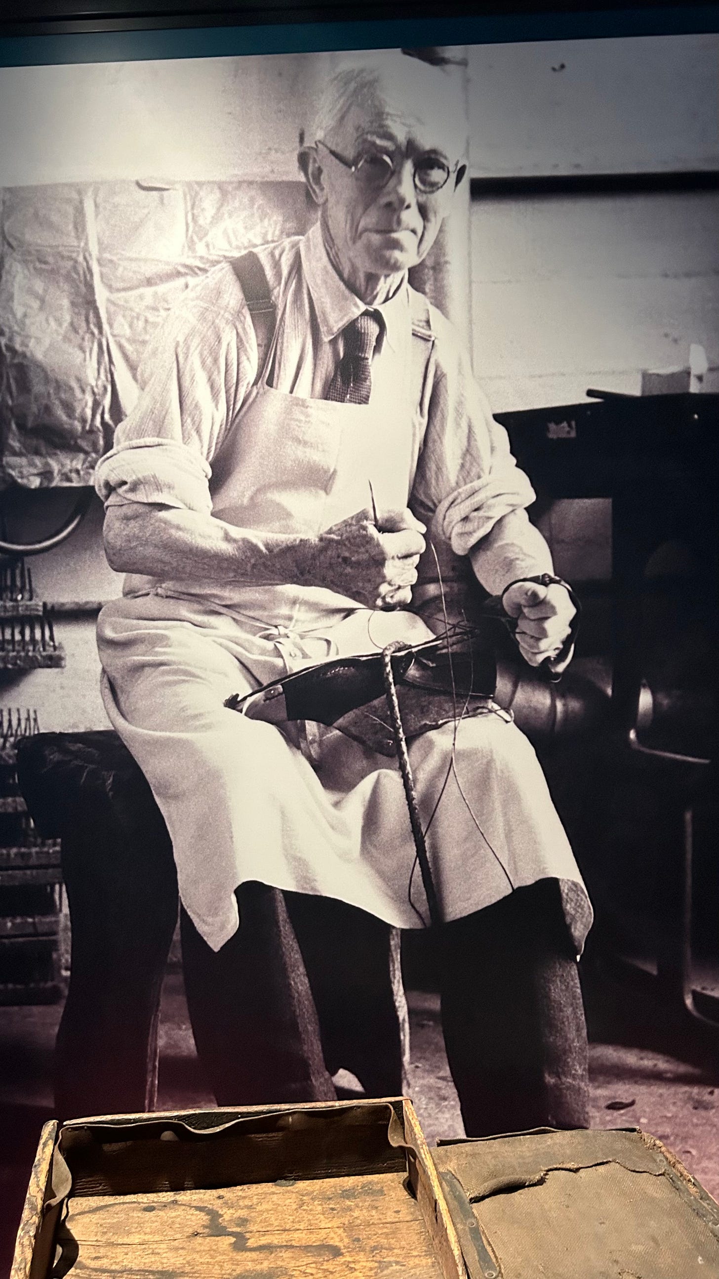 A photo of Alf White who worked for Clarks from age 10. Wearing has apron in older age he is sat working making shoes. A photo of Alf White who worked for Clarks from age 10. Wearing has apron in older age he is sat working making shoes.