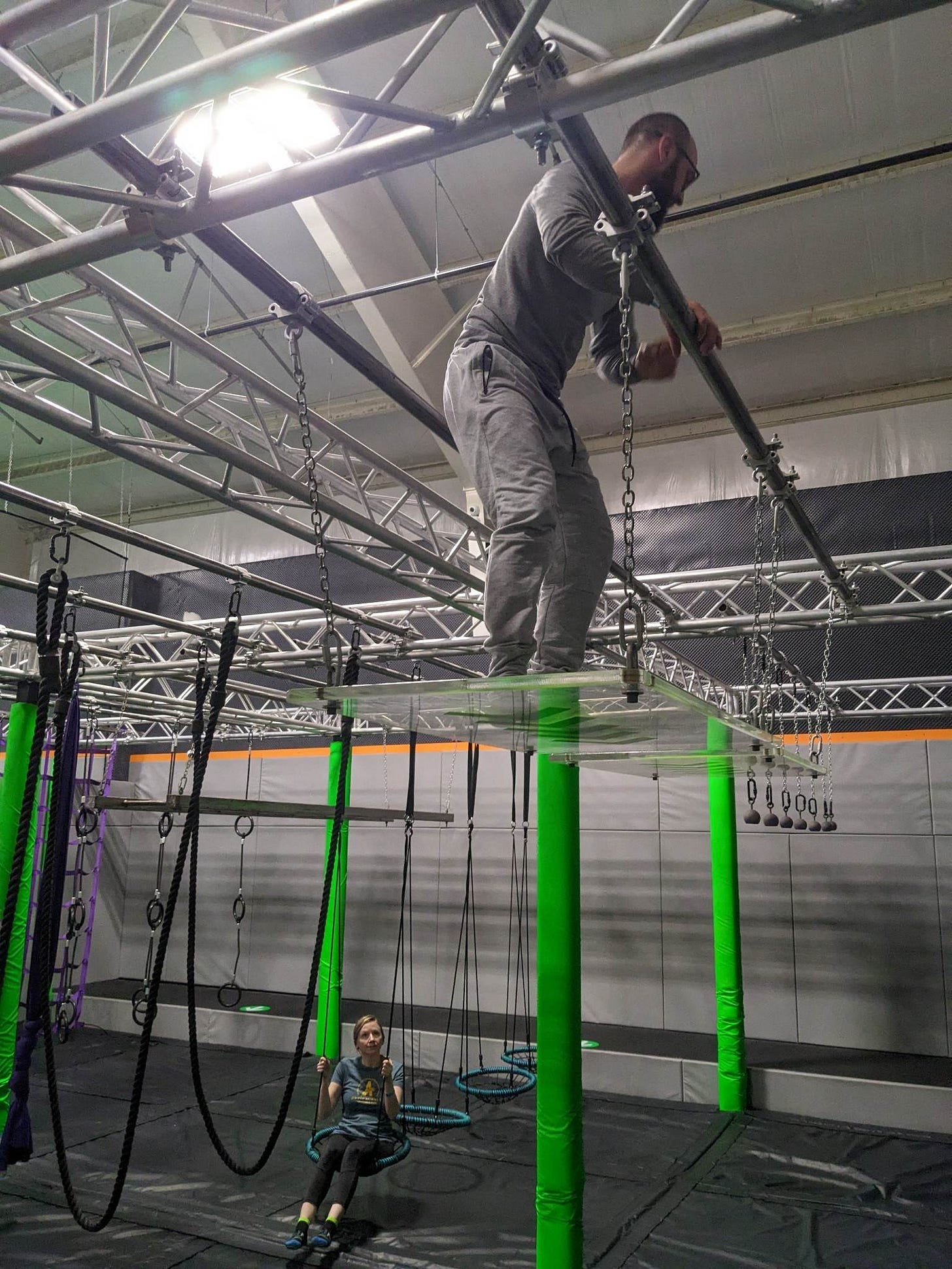 A woman watching a man climb a Ninja Warrior Course