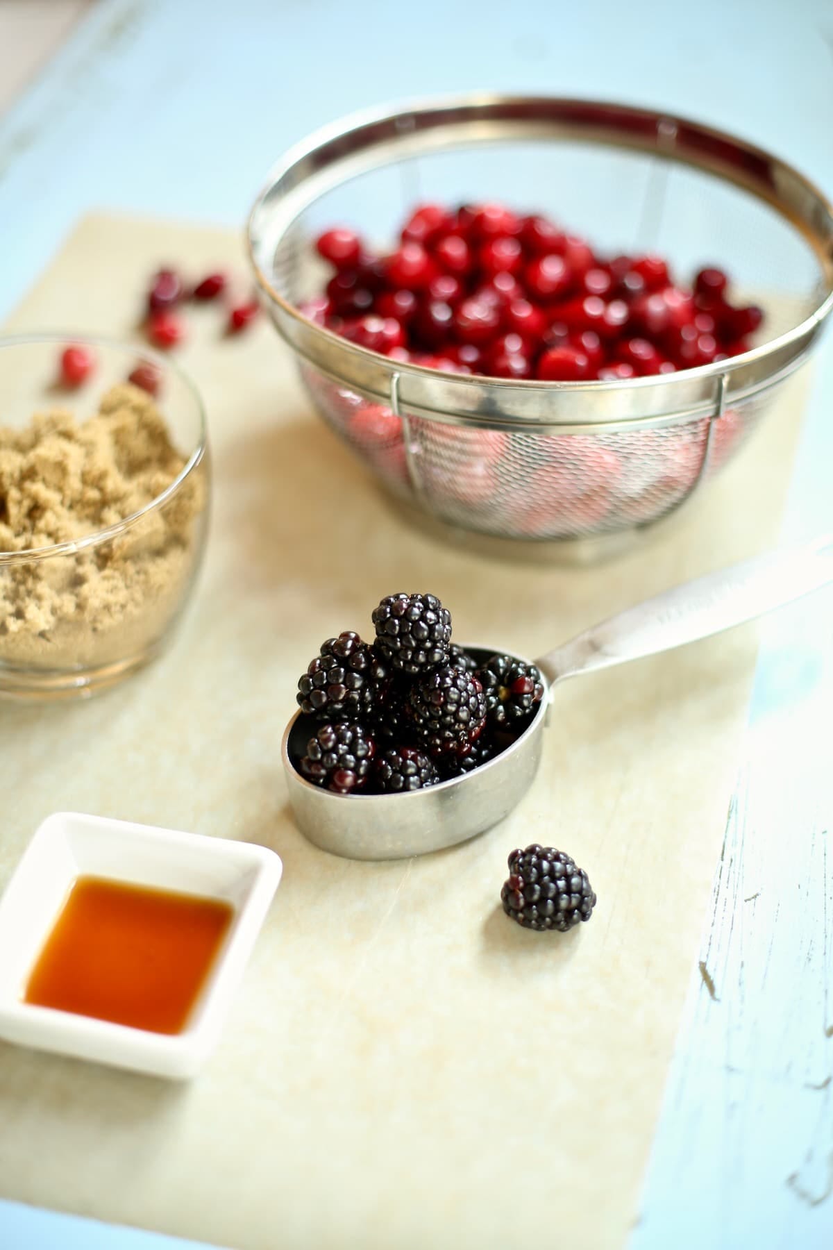 fresh blackberries in a silver measuring cup, with a glass cup of brown sugar next to it and a wire colander of cranberries behind it.  fresh blackberries in a silver measuring cup, with a glass cup of brown sugar next to it and a wire colander of cranberries behind it.