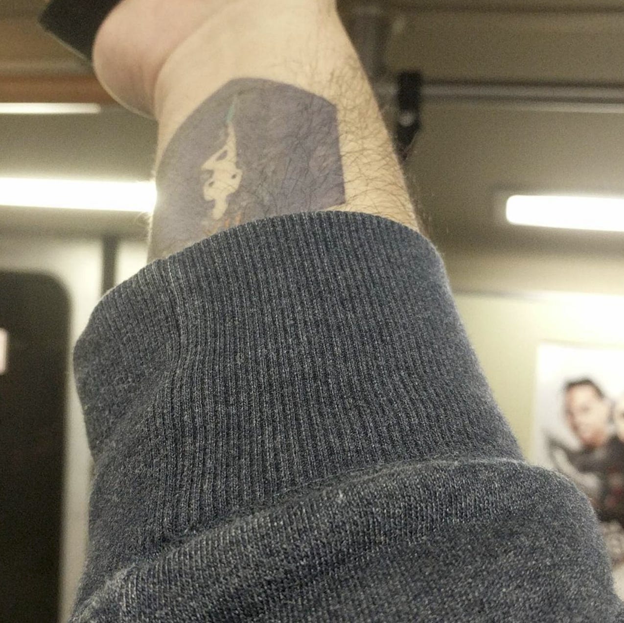 A tattoo of the Hanged Man Arcana on the wrist partially obscured by a hoodie.
