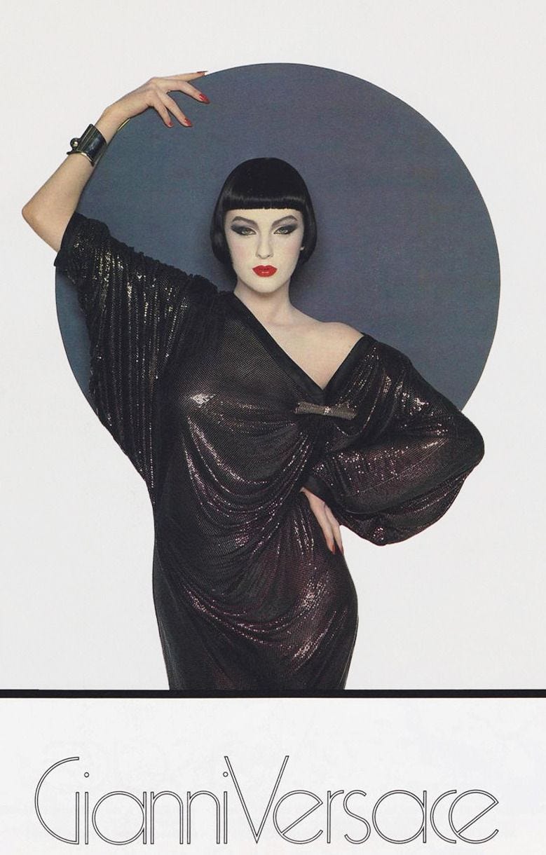 A model wearing a dark chainmail dressstands before an art deco-like orb feature.