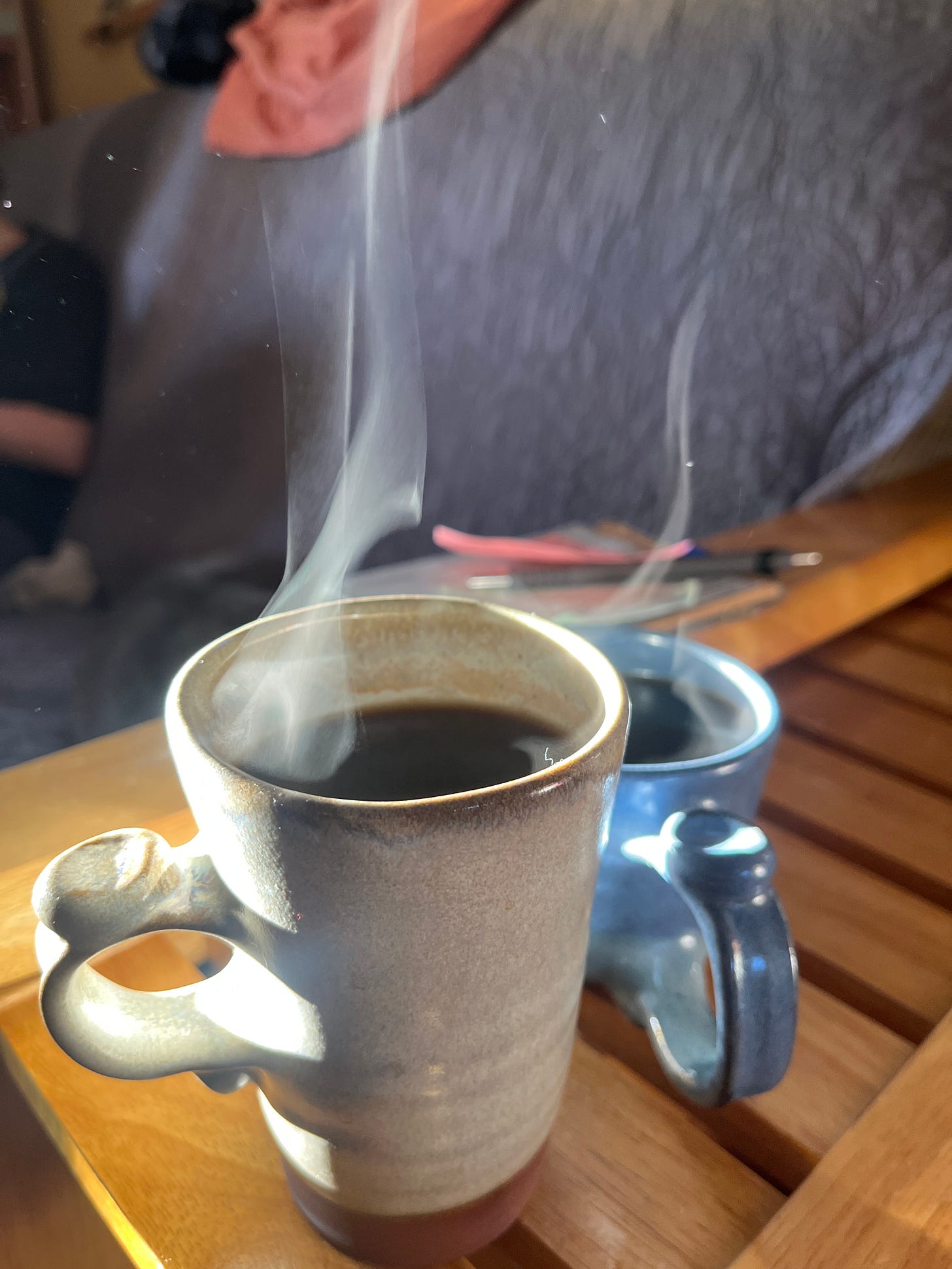 Two mugs of hot coffee sitting on a little shelf by our couch. The morning light catches them in a way you can really see the steam coming off the mugs like smoke