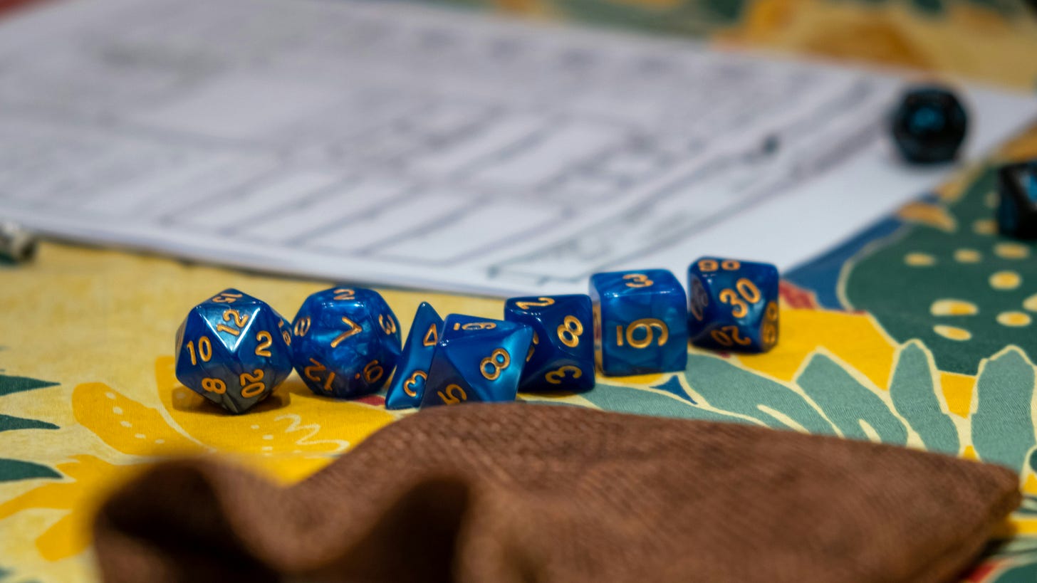 A set of blue D&D dice on a tabletop, with a character sheet visible in the background