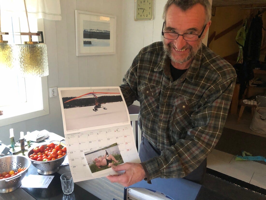 A man in a kitchen, smiling, presenting a calendar page. A man in a kitchen, smiling, presenting a calendar page.