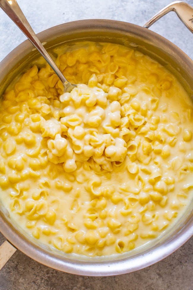 A scoop of white cheddar mac and cheese being lifted from a pot. A scoop of white cheddar mac and cheese being lifted from a pot.