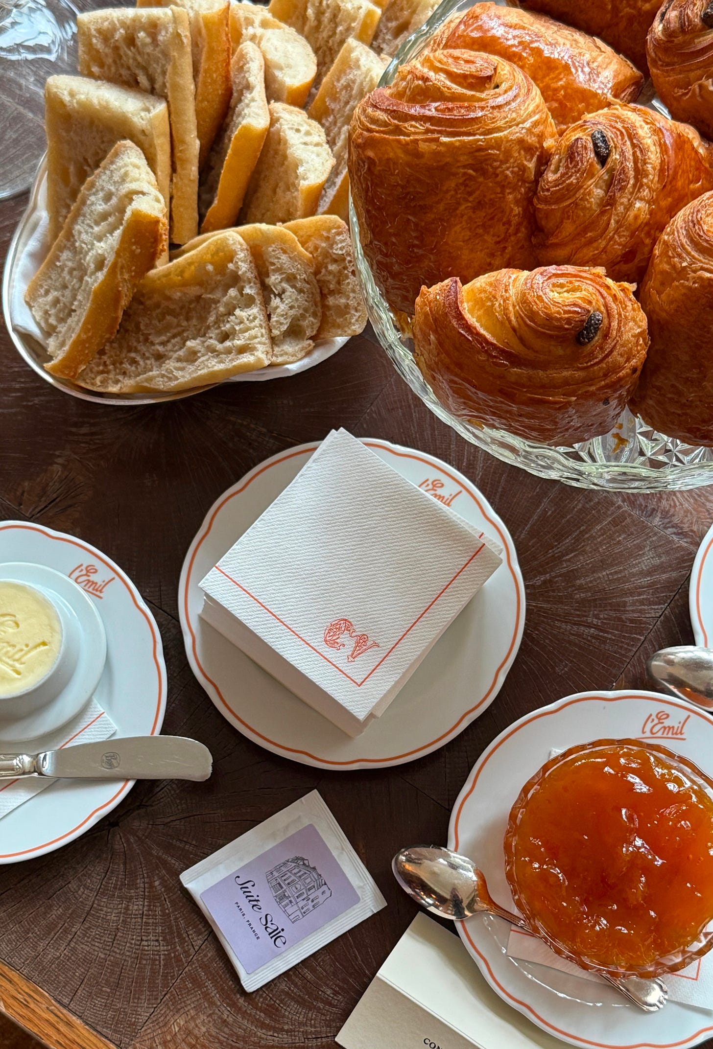 Trays of pastries and baguettes with jam, butter, and napkins on the side.