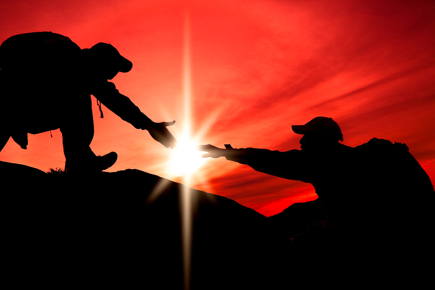 Two people climbing with the sun behind them with one reaching out to help the other Two people climbing with the sun behind them with one reaching out to help the other