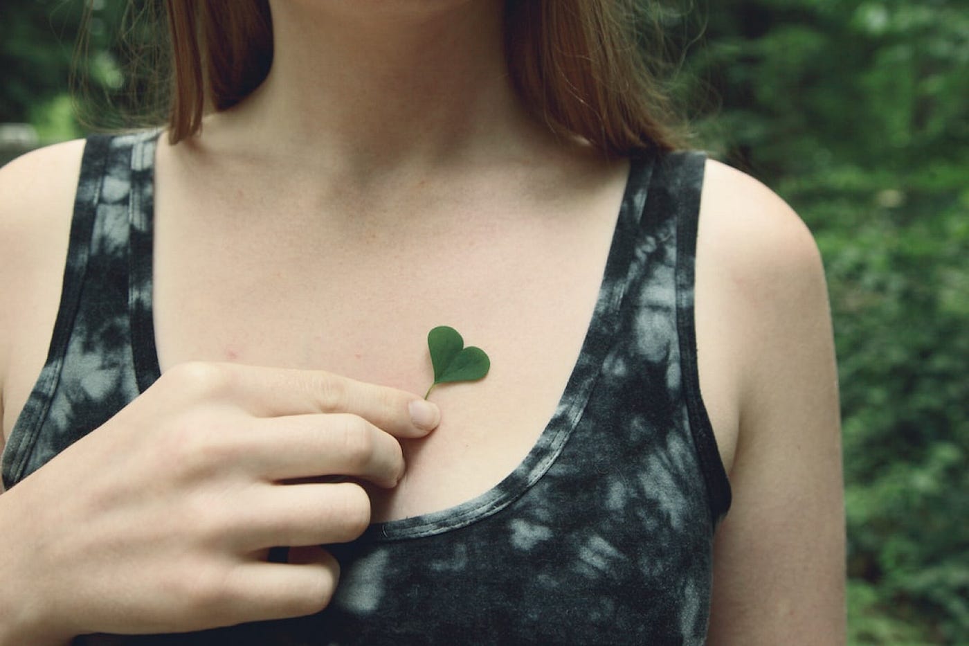 Photo of woman’s upper torso holding a heart-shaped clover.