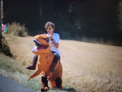 Image of a chateau on a mountain, a fan with an Alaphillippe sign, a fan wearing a t-rex costume