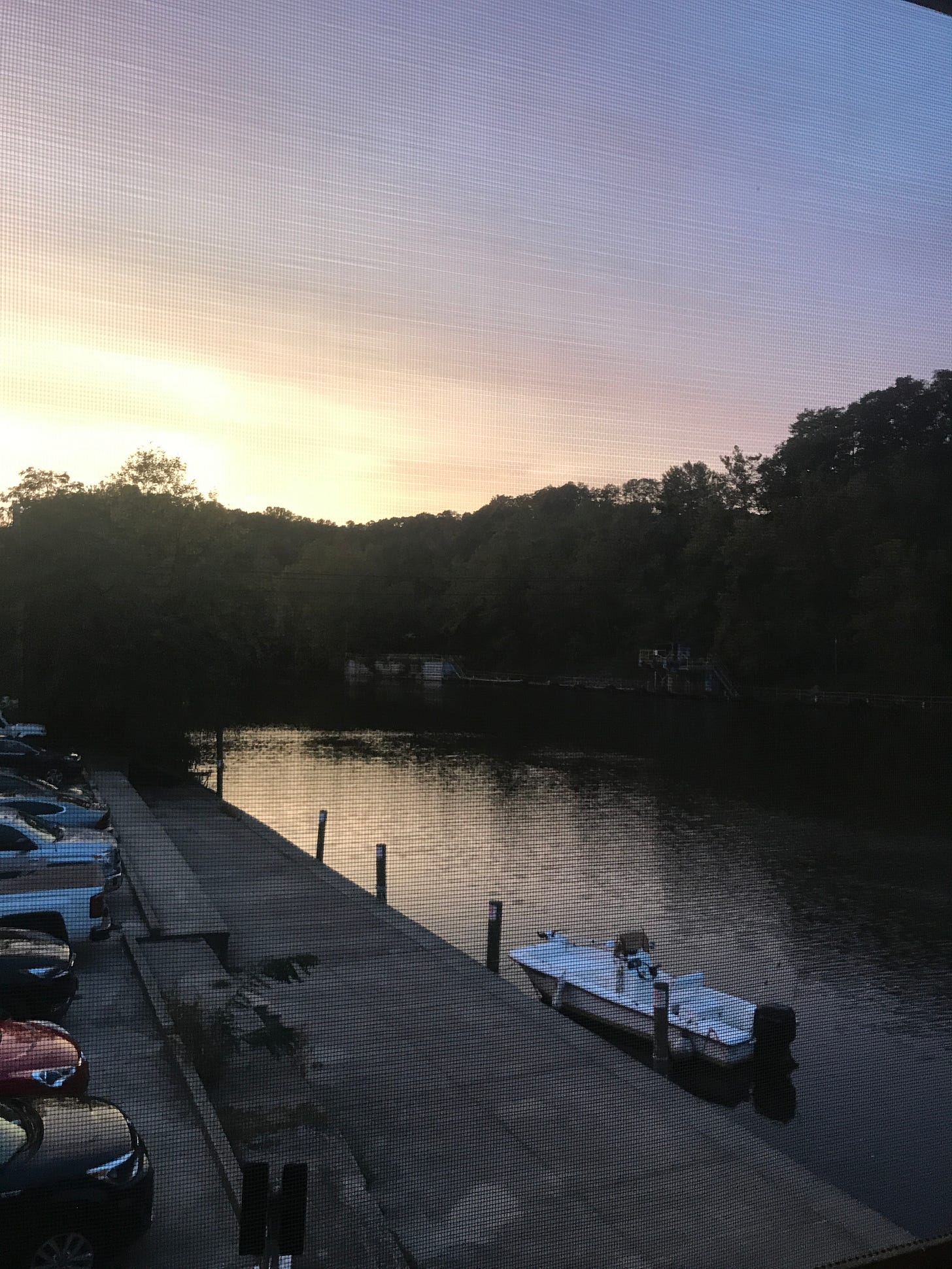 The occoquan river at sunset. Cars are parked on the pavement on one side of the river, the other is trees. A white motorboat is docked.