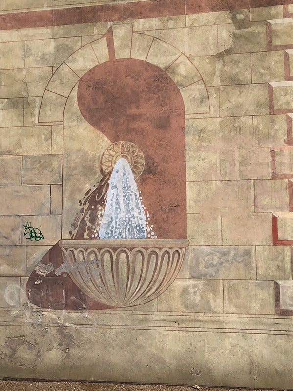 Old mural on side of building showing a water fountain.