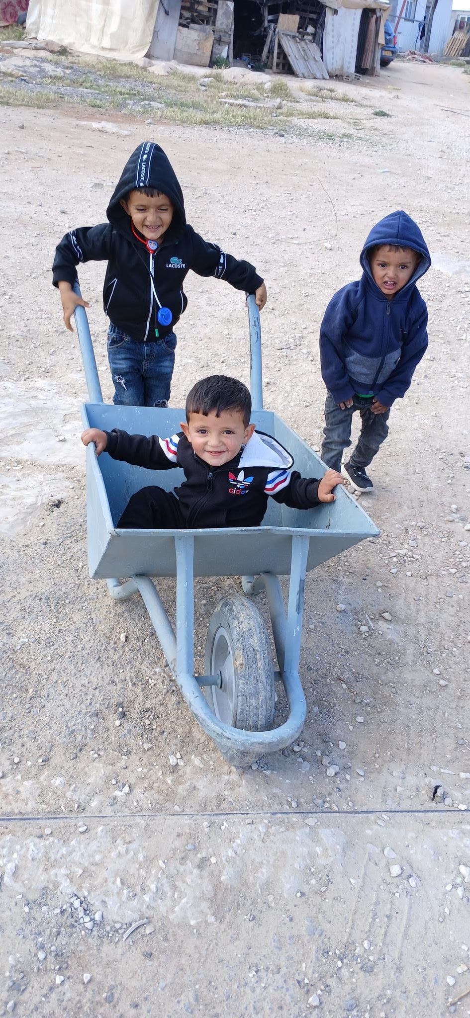 Three Palestinian children playing with a wheelbarrow. 