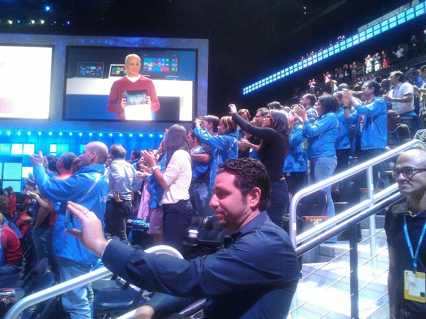 A photo of the big screens at an event with me on stage showing Surface. In the photo is Panos taking a phot oof the stage with Satya behind him. A photo of the big screens at an event with me on stage showing Surface. In the photo is Panos taking a phot oof the stage with Satya behind him.