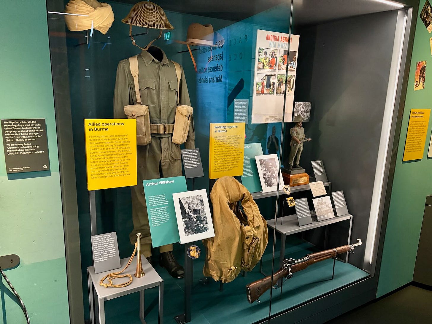 Exhibit on Allied operations in Burma at IWM London, featuring informational panels, photographs, a military uniform, and a displayed gun.