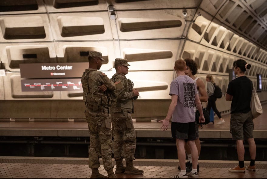 Two National Guard members, dressed in fatigues, speak with three young adults inside the DC Metro Center.