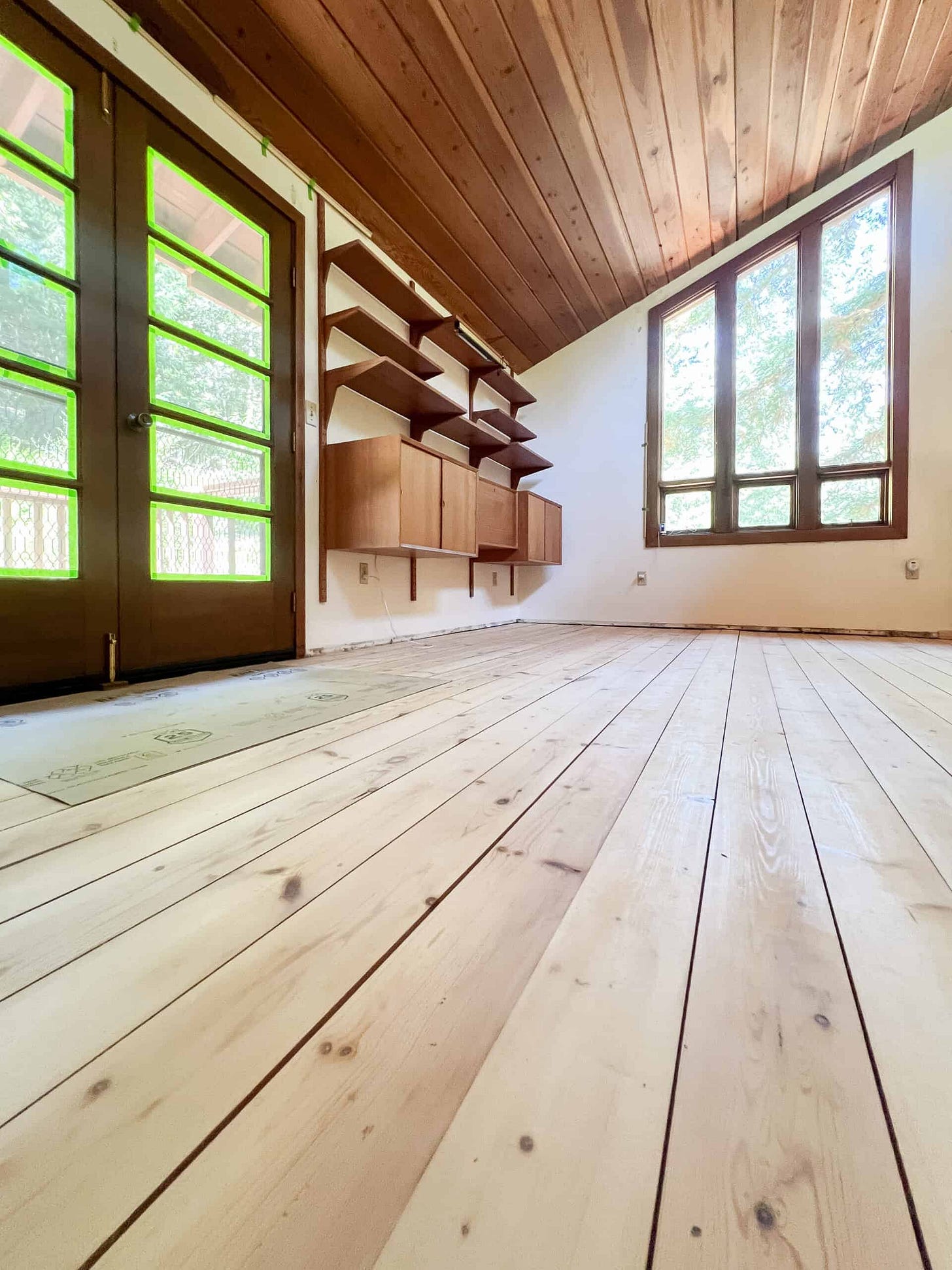 Hardwood pine floors freshly sanded with red wood ceilings and a wall mounted display unit empty.