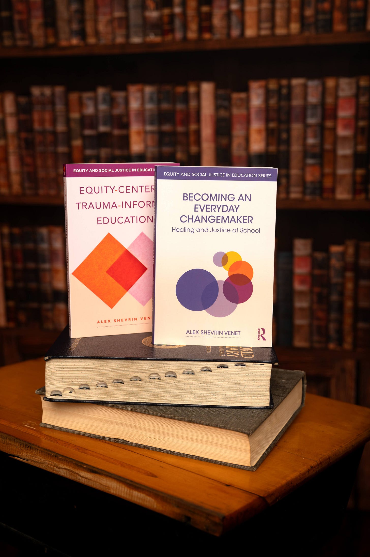 the books Equity-Centered Trauma-Informed Education and Becoming an Everyday Changemaker displayed in front of a library wall 