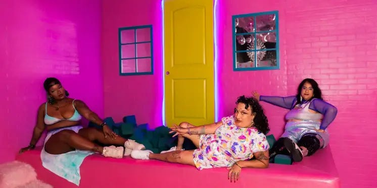 3 disabled artists lounge in what looks like it could be the inside of Barbie’s Dreamhouse.