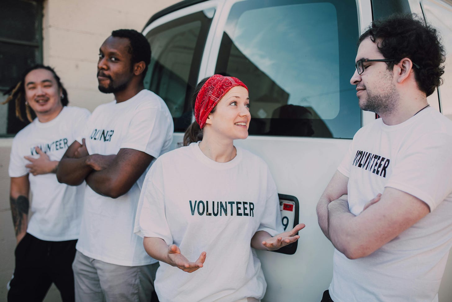 Four volunteers engaging in conversation beside a van during a community service event. Four volunteers engaging in conversation beside a van during a community service event.