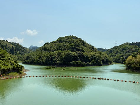 views of a deep-green reservoir surrounded by trees and fields far below on the other side of the dam