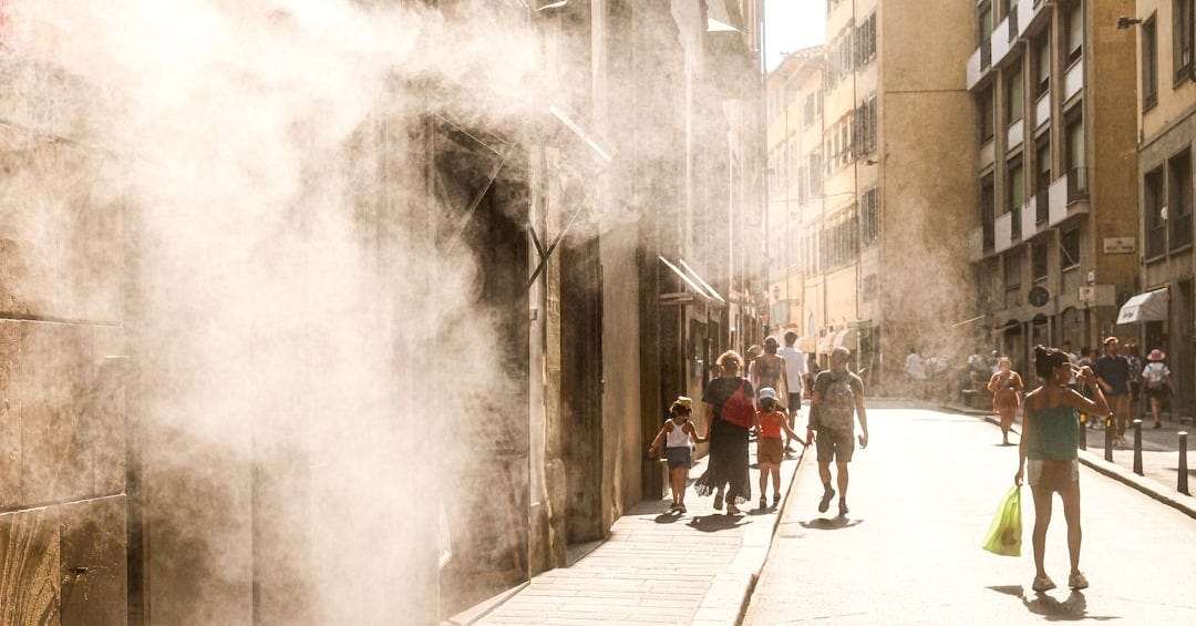 People walk down a sunny street with misting spray.