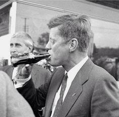 This may contain: a man in a suit drinking from a bottle while standing next to another man wearing a tie