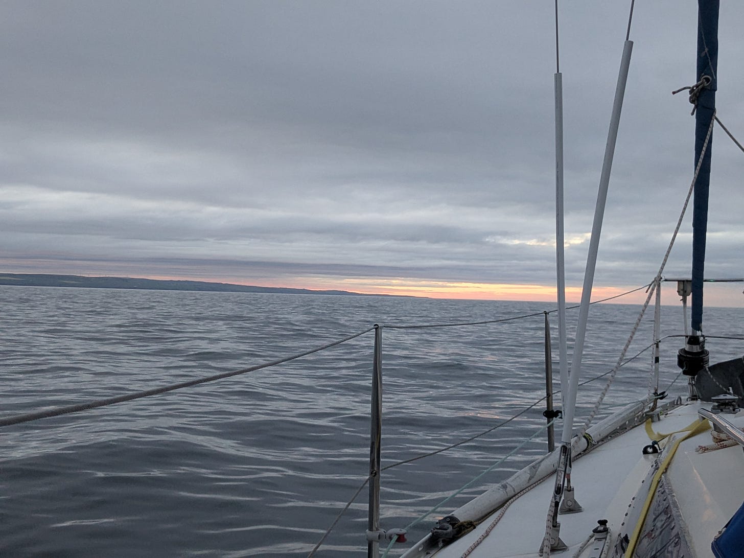 Looking over the bow of the boat towards the setting sun of the northern Scottish coast a yellow glow on the horizon under the clouds