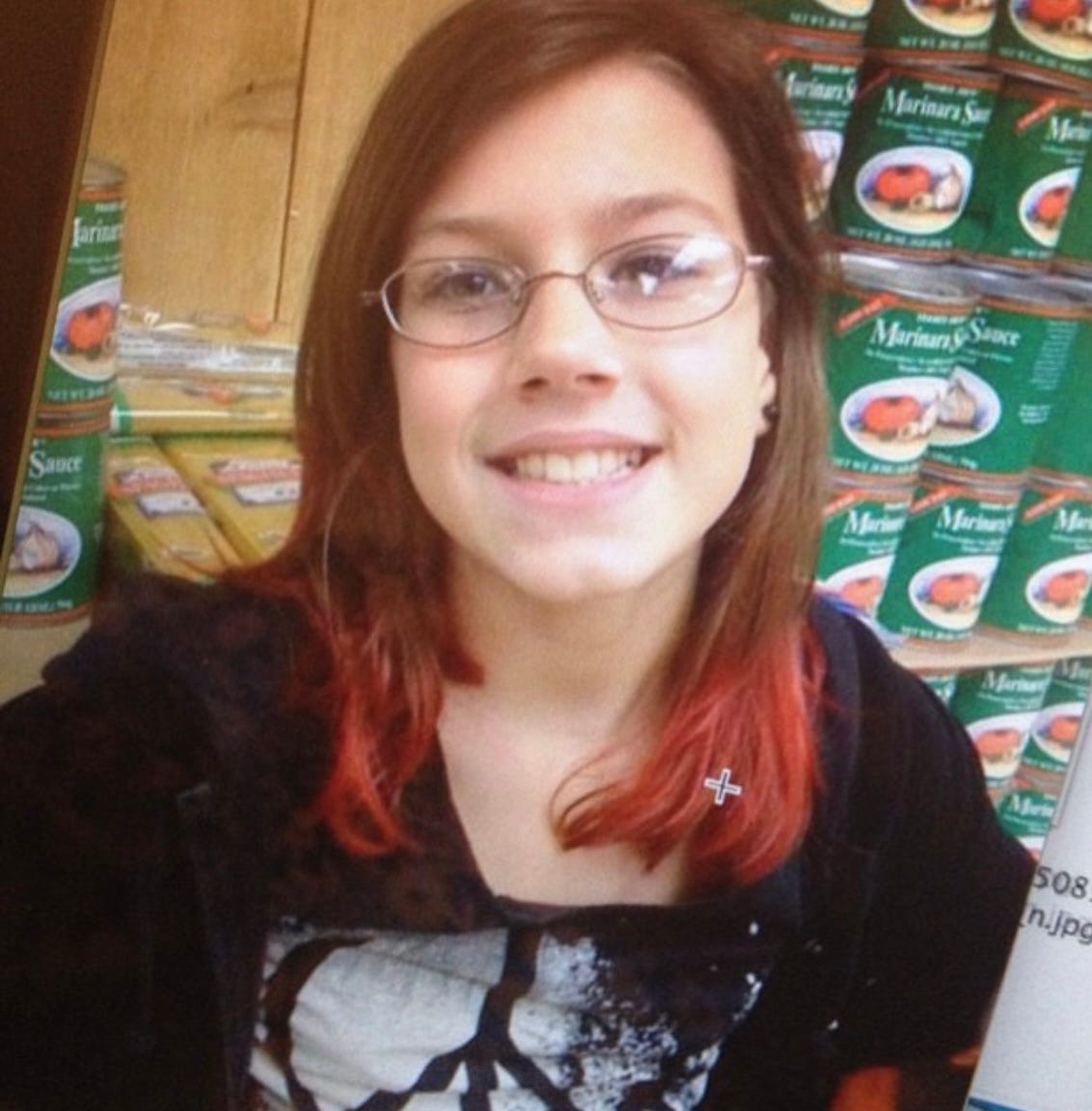 image of the author when they were 11 posed in a trader joes in front of a wall of canned tomatoes smiling showing off their red dip dyed hair. they have thin wire rimmed glasses