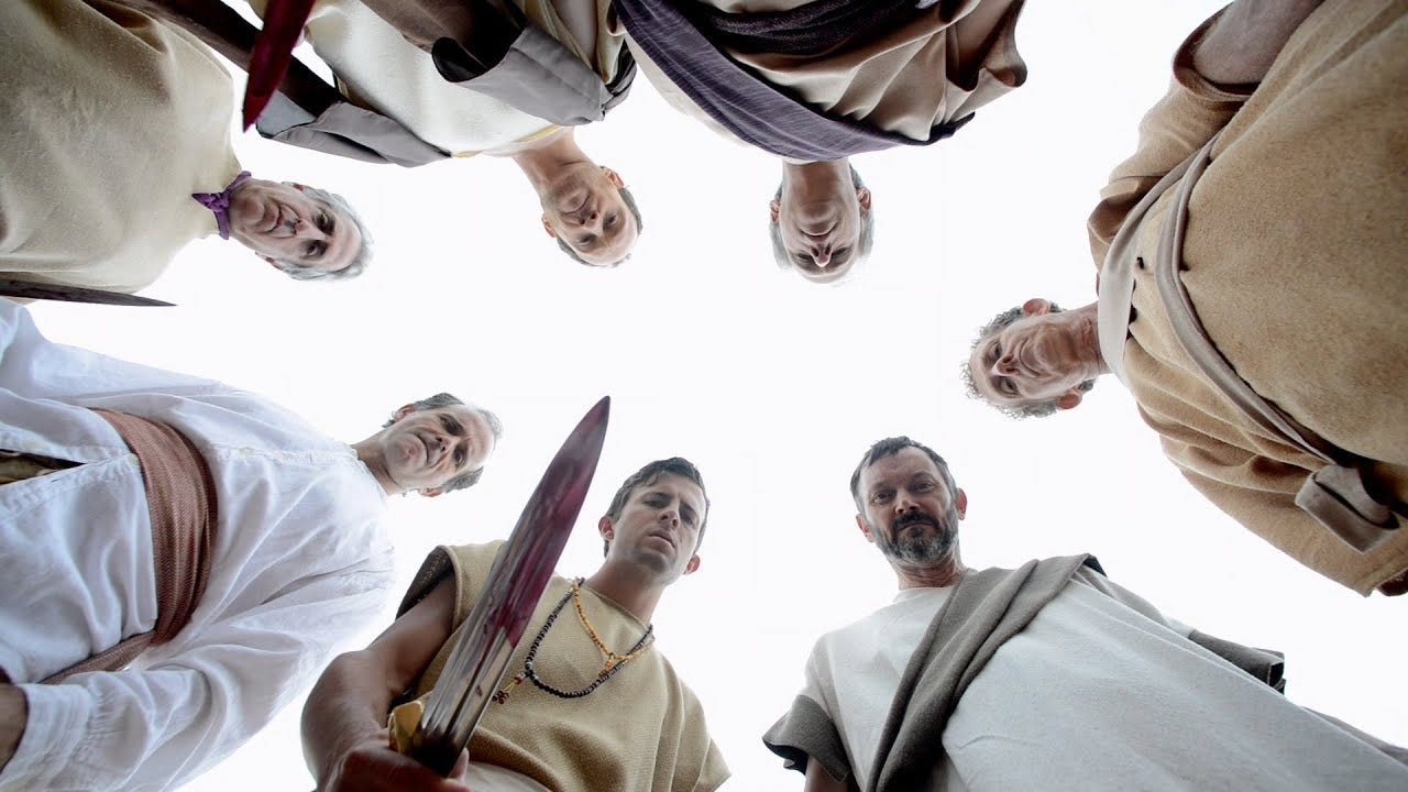 A corpse's-eye view of seven murderers looking down at their victim.