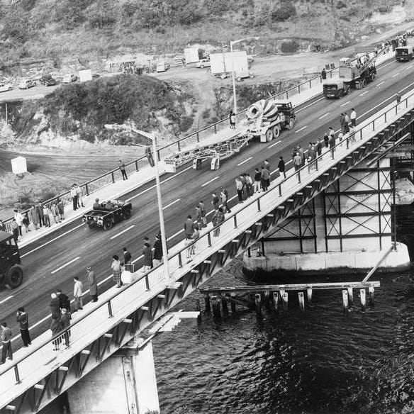 Left: A view from the river, looking up to the bridge - it's painted blue and has a white handrail on the footpath. There is one leg of the bridge going into the river itself. Right: An aerial view of the bridge, in black and white, with lots of people standing on the footpath and traffic on the bridge. There is still scaffolding under the bridge.