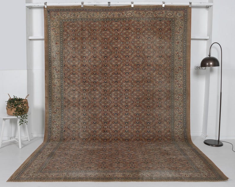 May include: A large, rectangular, antique rug with a detailed, repeating geometric pattern in shades of brown, beige, and blue. The rug has a wide border with intricate designs. The rug is displayed on a white background.