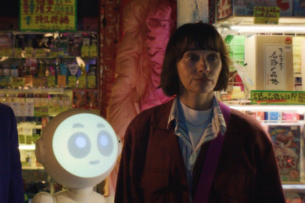 Sunny, a small white robot with an LED face, and Suzie (Rashida Jones) stood next to each other in a scene from Apple TV+ series Sunny