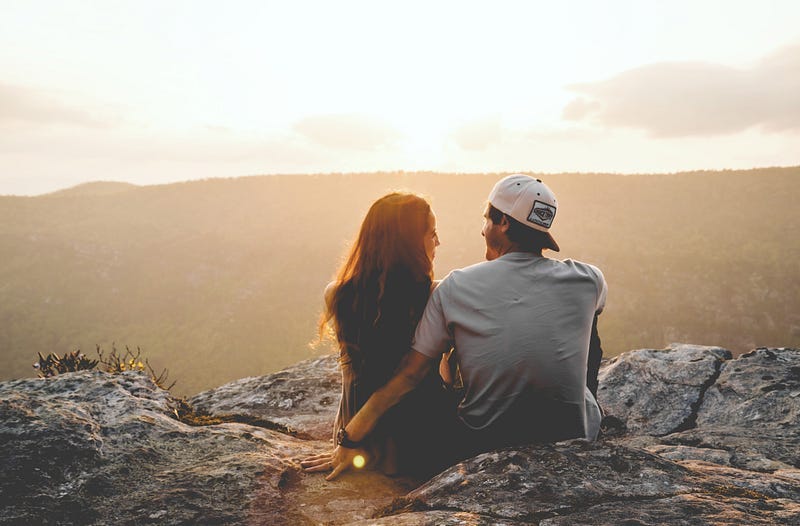 a couple sitting on the ground, overlooking mountains a couple sitting on the ground, overlooking mountains