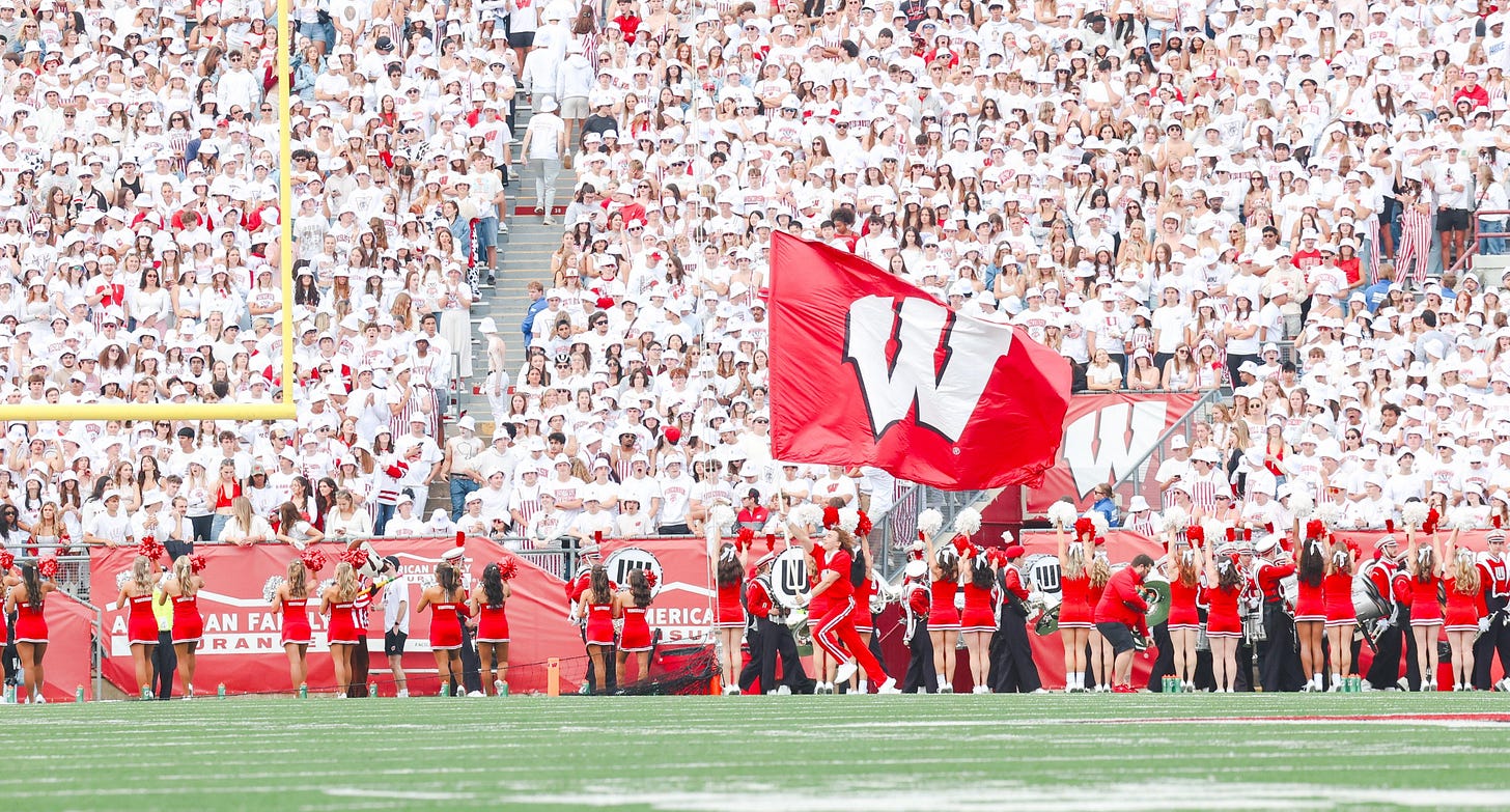 Wisconsin cheerleader running the Badgers flag across the field during a home game at Camp Randall Stadium.