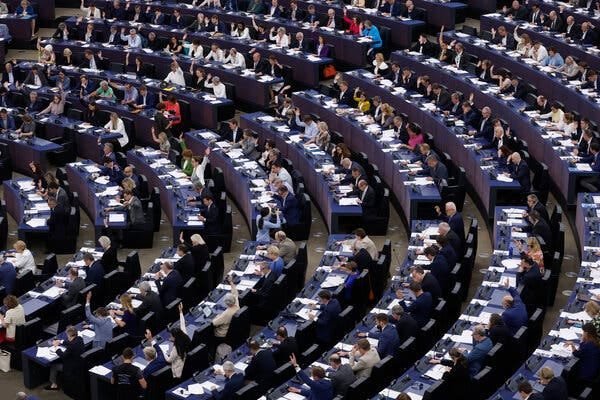 People sitting in semicircular rows, with white papers on the desks in front of them.