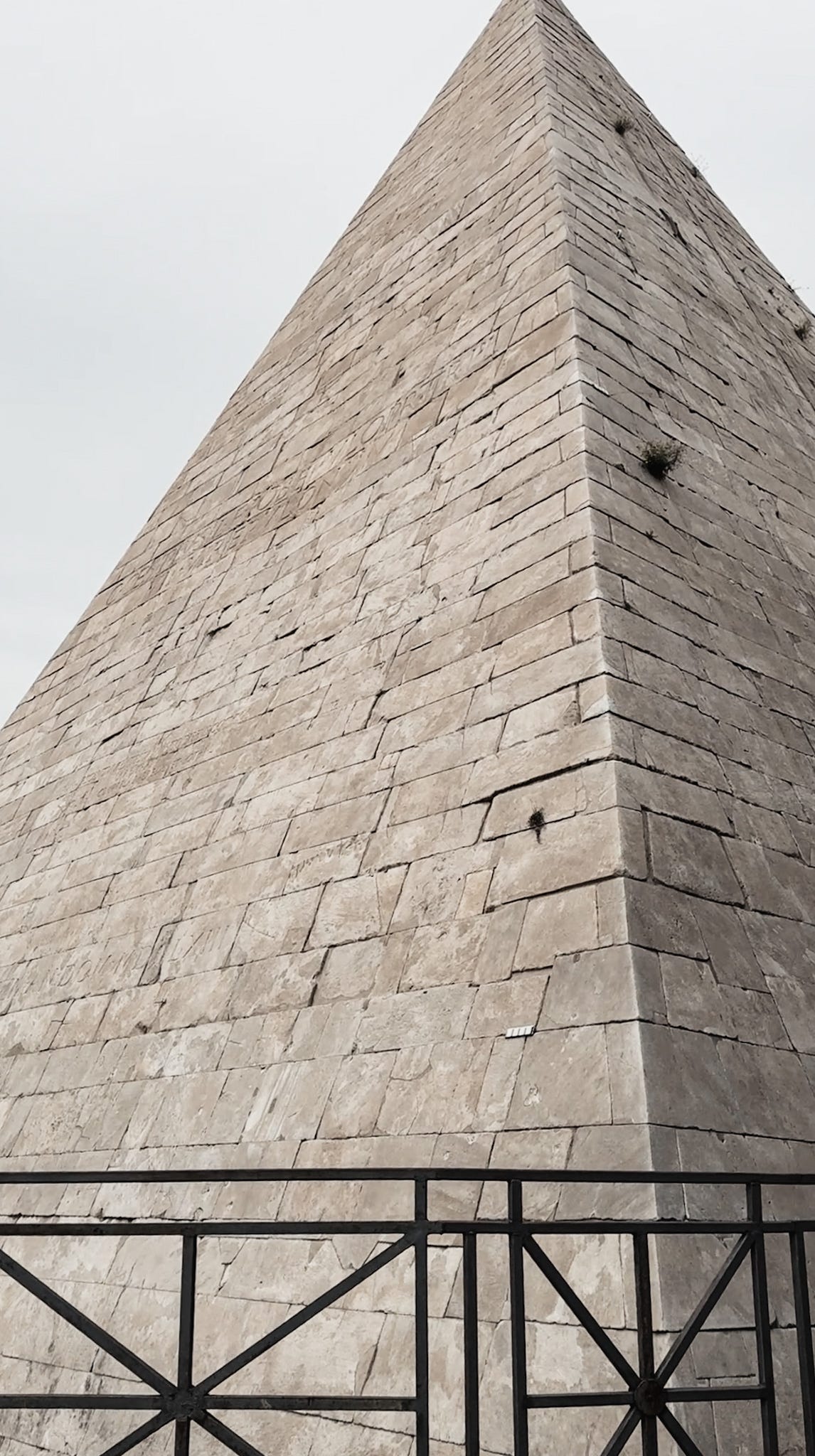 A minimalist perspective of the Pyramid of Cestius in Rome, showing its sharp triangular form with modern scaffolding at the base—an ancient monument framed through a contemporary lens.