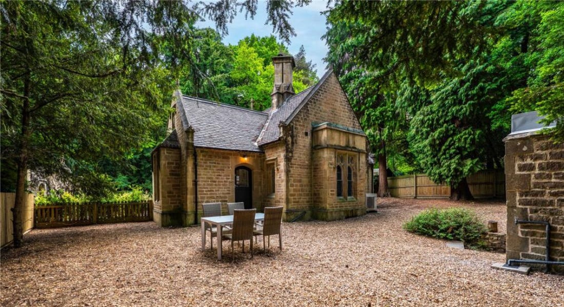 A brown brick gothic home with stone in front of it, a dining table set, and trees around it